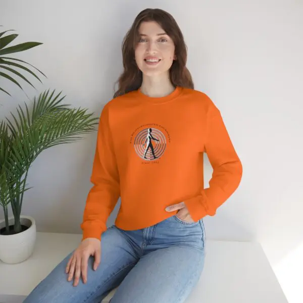 A woman sitting on the ground wearing an orange sweatshirt.