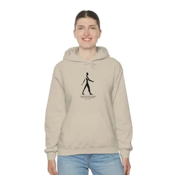 A woman wearing a beige hoodie with an image of a person walking.