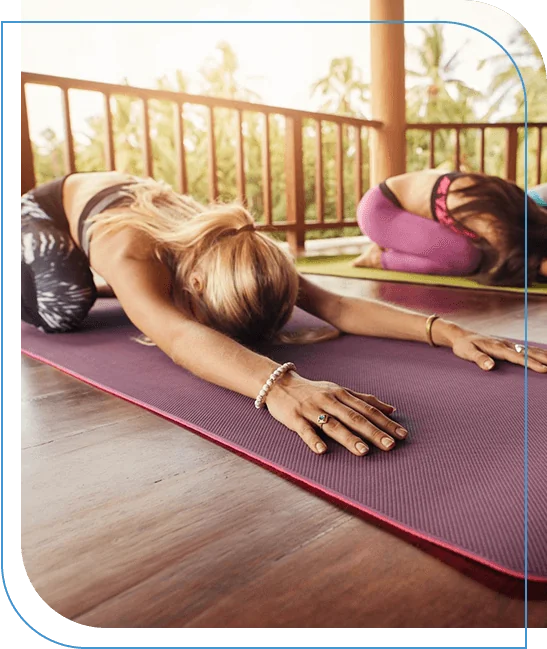 Two women practicing classical Pilates stretches on mats in a bright studio.